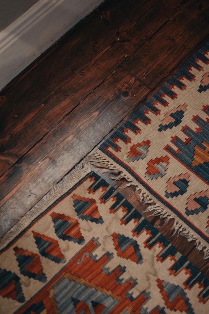 Detailed close-up of a colorful geometric patterned rug on a wooden floor with muted lighting.